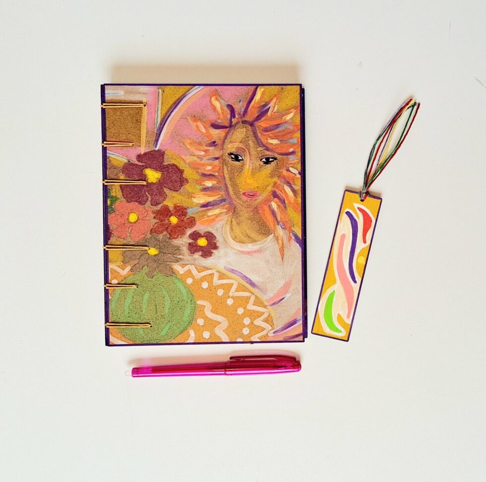 Carnet SUZANA recto, accompagné d'un stylo rose et d'un marque-page en bois disposé à côté.