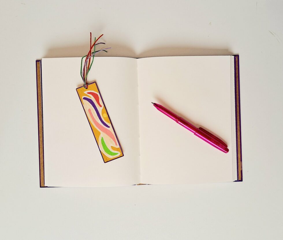 Carnet SUZANA ouvert sur pages intérieures avec stylo rose et marque page en bois disposé à côté.