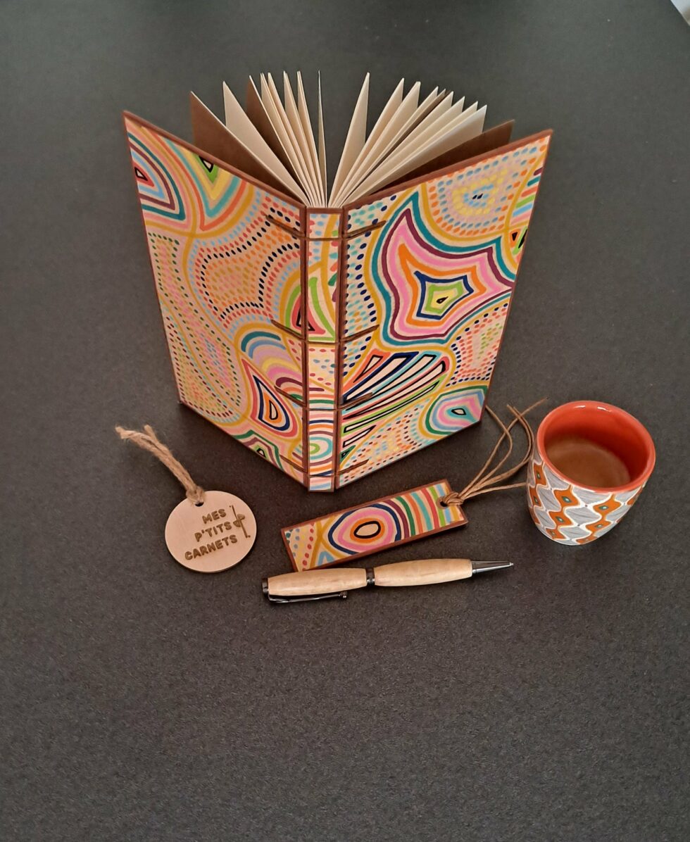 Carnet KIMBA, vue recto verso debout avec marque-pages en bois peint à la main et stylo en bois peint.