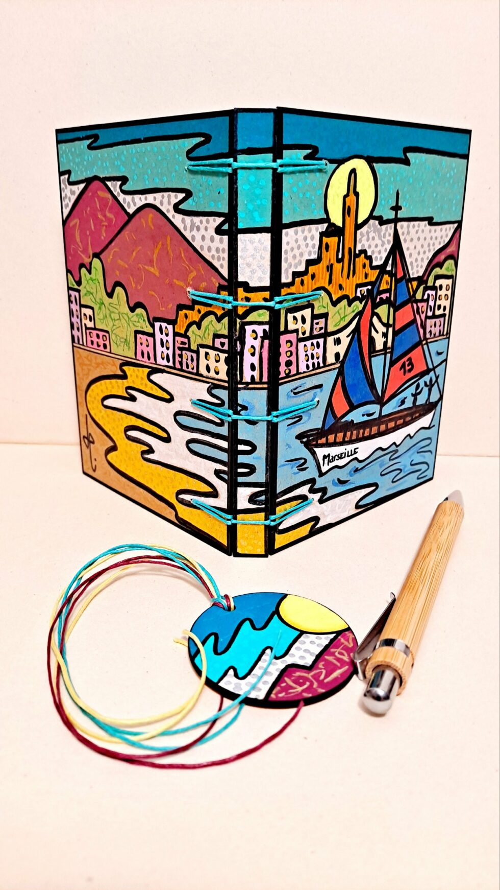 Carnet RÉGATE vue ouverte couverture debout avec marque-pages et stylo en bois.