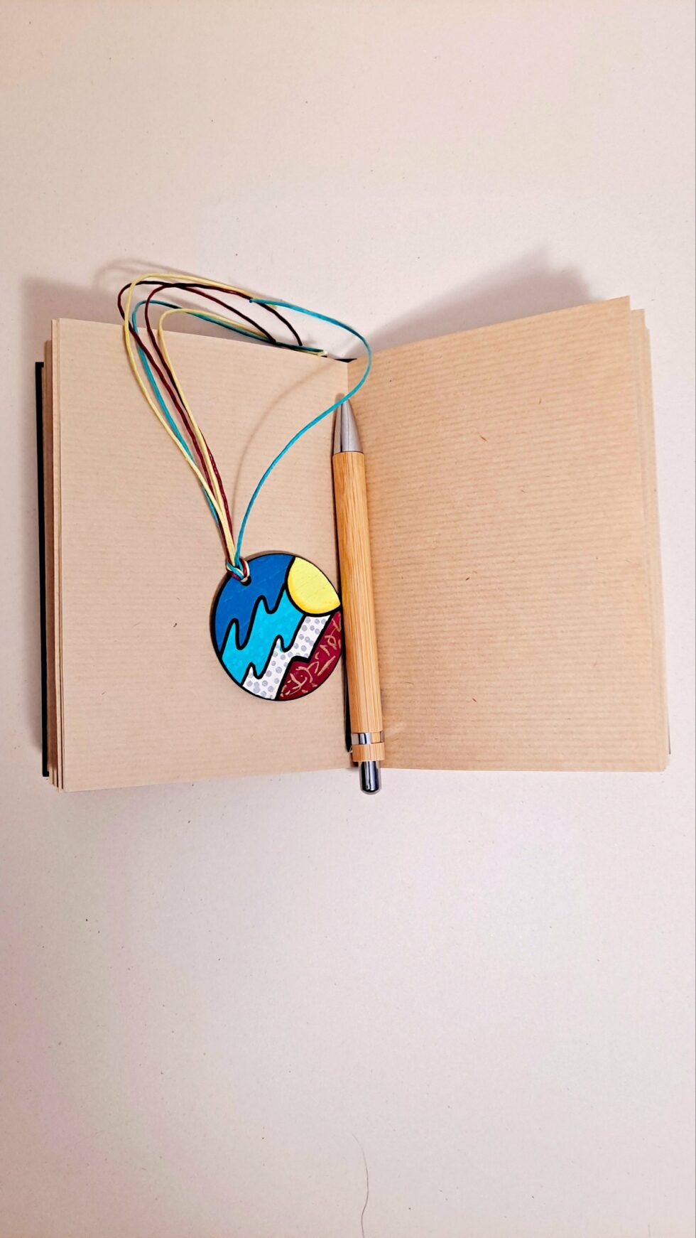 Carnet RÉGATE vue ouverte à plat sur pages avec marque-pages et stylo en bois.